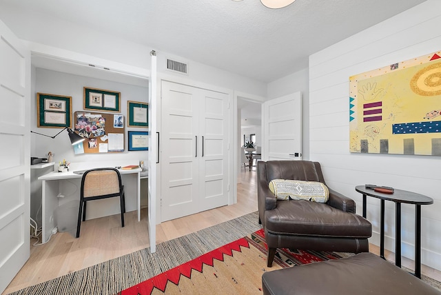 living area with a textured ceiling, wood-type flooring, and wooden walls