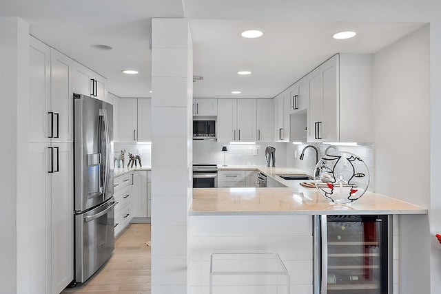 kitchen with wine cooler, backsplash, sink, stainless steel appliances, and white cabinets