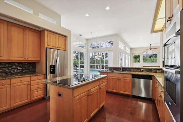 kitchen with a center island, stainless steel appliances, dark hardwood / wood-style flooring, dark stone countertops, and sink