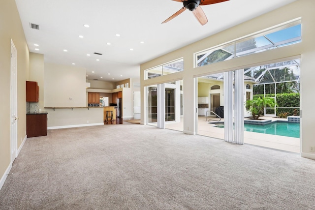 unfurnished living room featuring a towering ceiling, ceiling fan, light carpet, and plenty of natural light