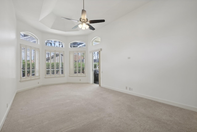 spare room featuring a raised ceiling, ceiling fan, and light colored carpet