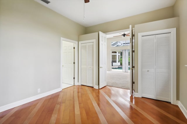 unfurnished bedroom featuring two closets, ceiling fan, and wood-type flooring