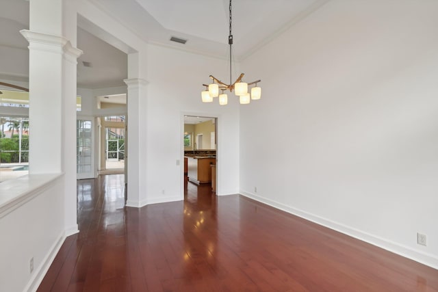 unfurnished dining area featuring dark hardwood / wood-style flooring, crown molding, a chandelier, and ornate columns