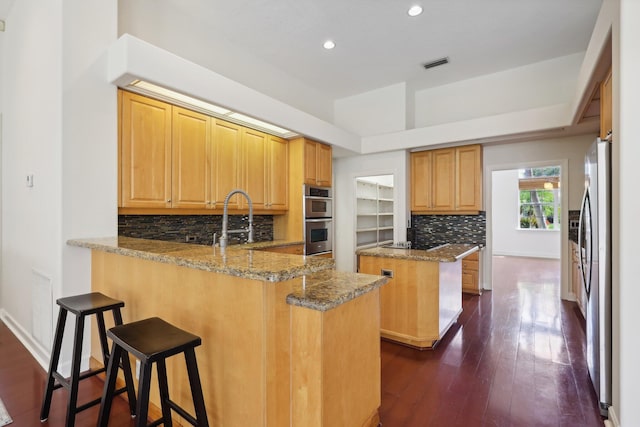 kitchen with stainless steel appliances, a center island, a kitchen bar, kitchen peninsula, and light stone countertops