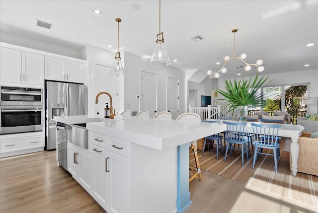 kitchen featuring hanging light fixtures, a center island with sink, white cabinetry, appliances with stainless steel finishes, and sink