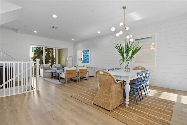 dining area with an inviting chandelier, wood walls, and light hardwood / wood-style flooring