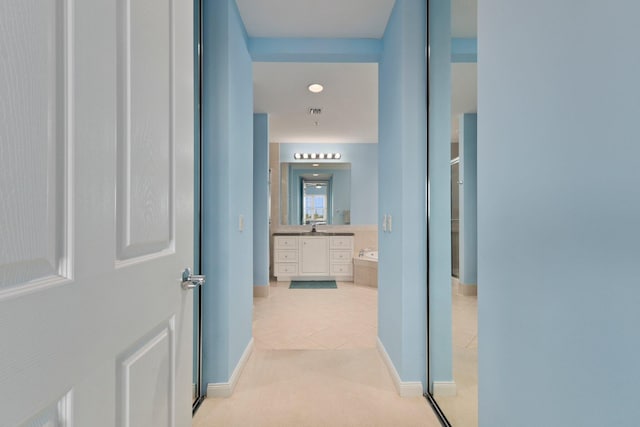 hallway featuring visible vents, a sink, baseboards, and light tile patterned floors