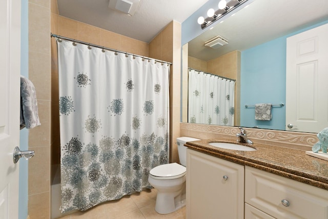 bathroom featuring tile patterned flooring, tiled shower, vanity, and toilet