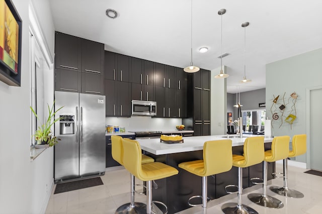 kitchen with pendant lighting, sink, appliances with stainless steel finishes, a kitchen island with sink, and a kitchen bar