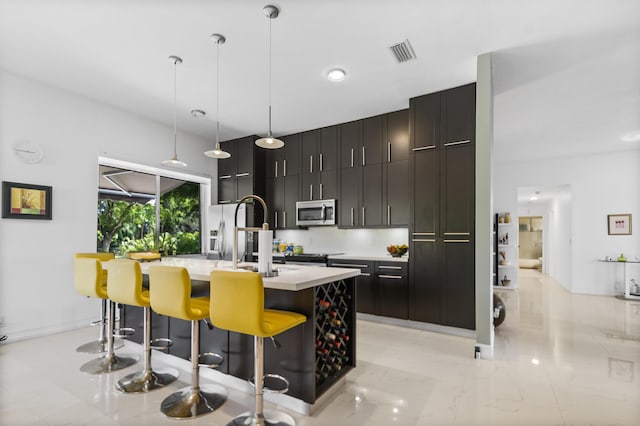 kitchen with a breakfast bar, sink, appliances with stainless steel finishes, an island with sink, and pendant lighting