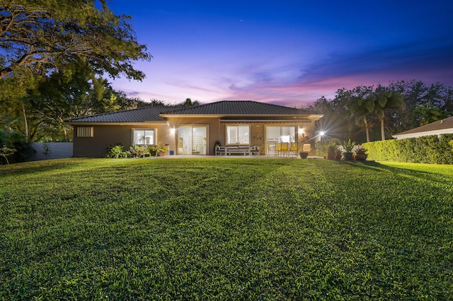 back house at dusk with a lawn and a patio area