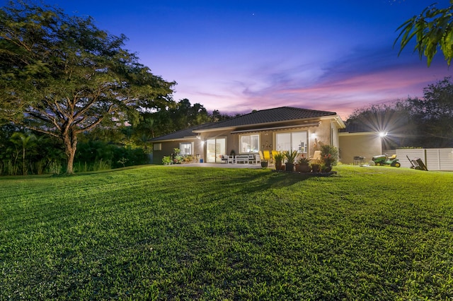 back house at dusk with a yard and a patio