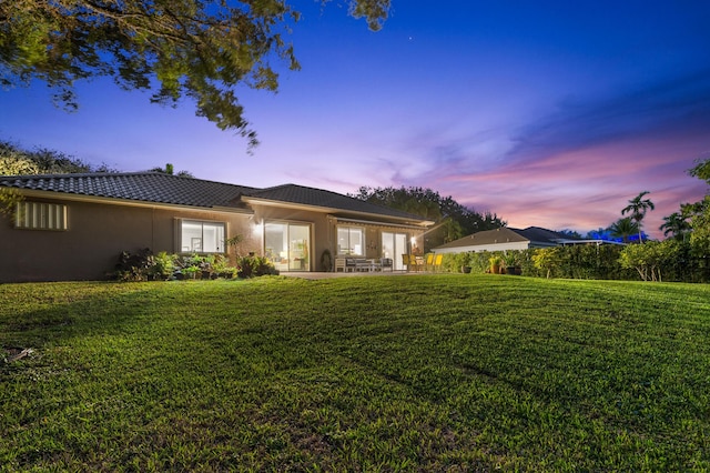 back house at dusk featuring a patio area and a lawn