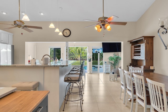 kitchen featuring light tile patterned floors, a breakfast bar area, ceiling fan, decorative light fixtures, and refrigerator