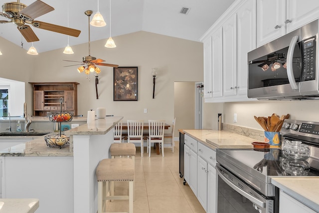 kitchen with light tile patterned floors, white cabinetry, stainless steel appliances, a kitchen breakfast bar, and vaulted ceiling