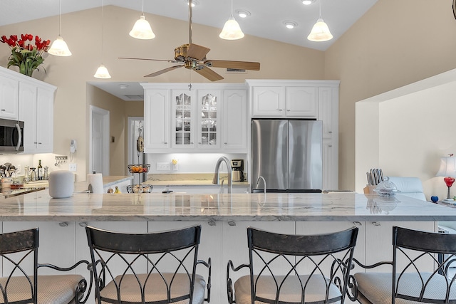 kitchen with pendant lighting, white cabinets, appliances with stainless steel finishes, vaulted ceiling, and light stone counters