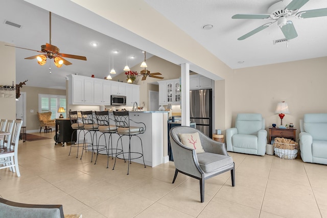 kitchen featuring a breakfast bar, light tile patterned flooring, stainless steel appliances, high vaulted ceiling, and white cabinets