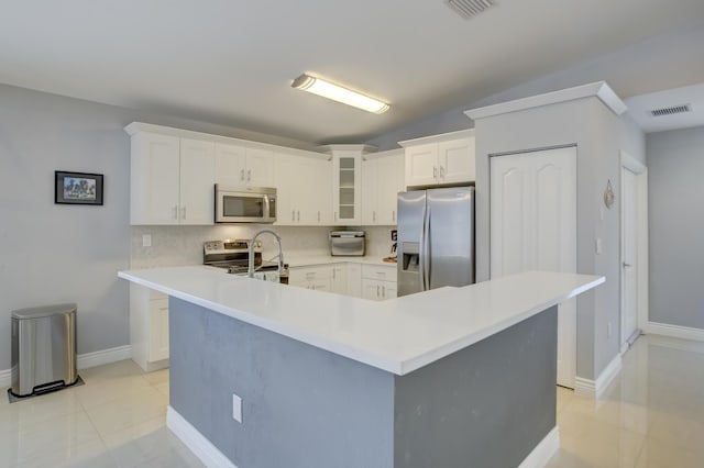 kitchen featuring lofted ceiling, tasteful backsplash, appliances with stainless steel finishes, a kitchen island with sink, and white cabinets