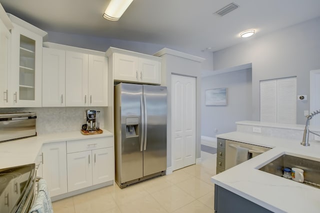 kitchen featuring appliances with stainless steel finishes, white cabinetry, sink, backsplash, and light tile patterned floors