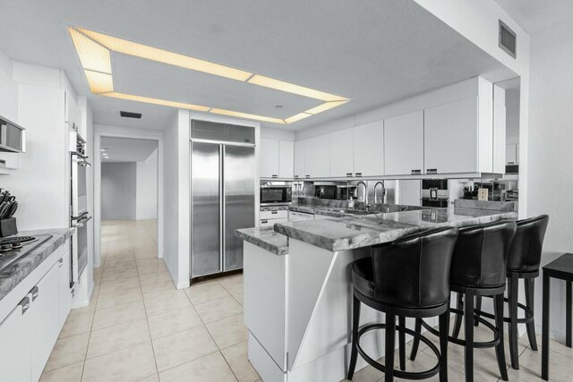 100 Lakeshore Dr Unit 252, North Palm Beach, FL 33408 - kitchen with white cabinets, a kitchen breakfast bar, kitchen peninsula, dark stone counters, and appliances with stainless steel finishes