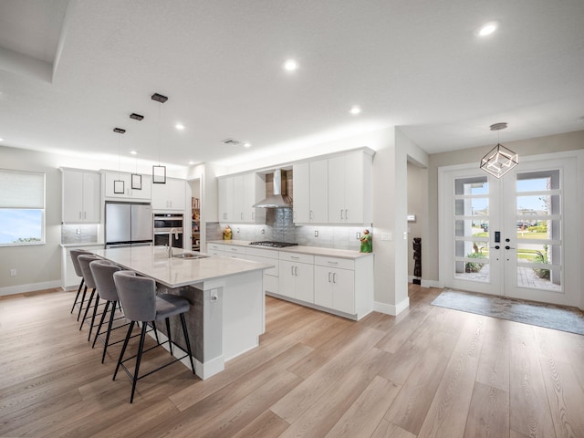 kitchen with white cabinetry, wall chimney exhaust hood, stainless steel appliances, and hanging light fixtures