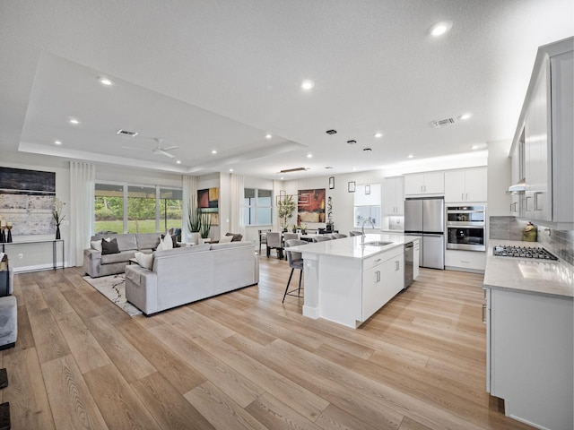 kitchen with a kitchen island with sink, sink, white cabinets, and a tray ceiling