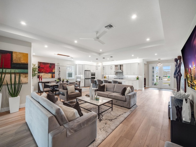 living room with ceiling fan, a raised ceiling, and light hardwood / wood-style floors