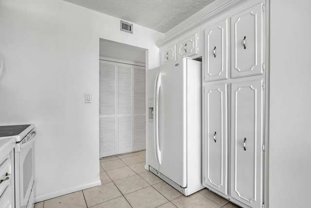 kitchen featuring white appliances, a textured ceiling, light tile patterned floors, and white cabinetry