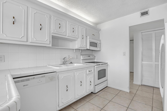 kitchen featuring sink, white cabinets, white appliances, light tile patterned floors, and tile counters