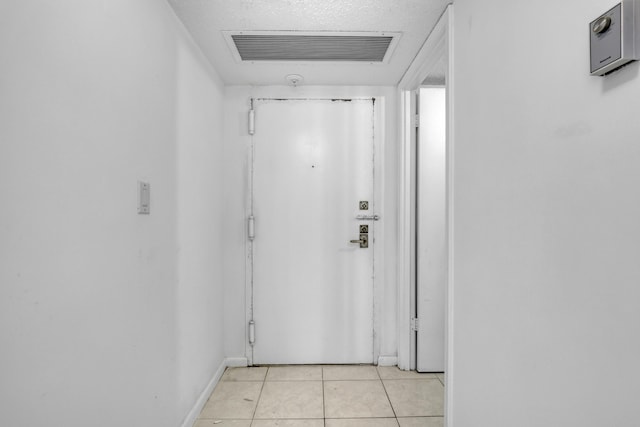 doorway to outside with a textured ceiling and light tile patterned floors