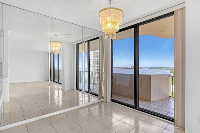 empty room with a water view, a healthy amount of sunlight, an inviting chandelier, and light tile patterned floors