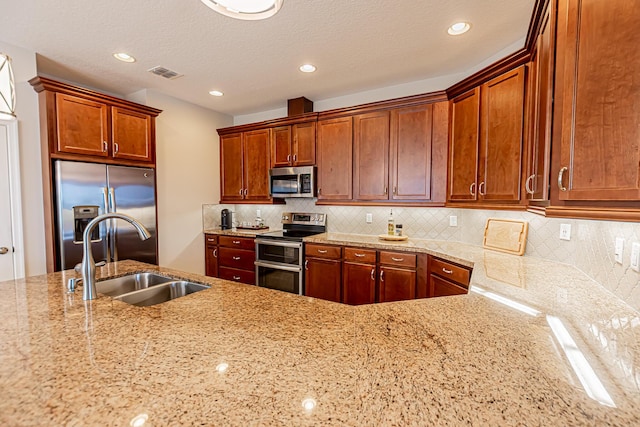 kitchen with appliances with stainless steel finishes, sink, light stone counters, and decorative backsplash