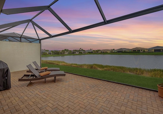 patio terrace at dusk featuring a grill, a water view, and glass enclosure