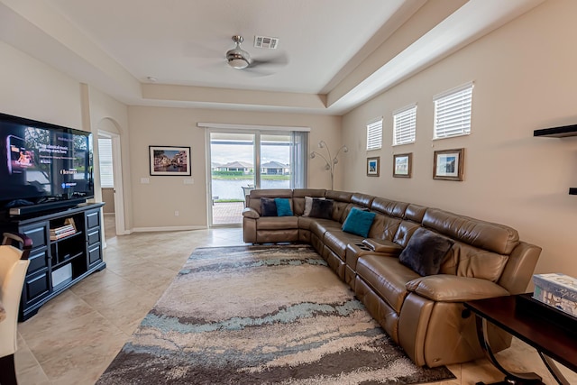 living room featuring ceiling fan, a tray ceiling, and light tile patterned floors