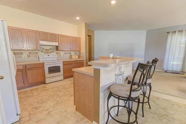 kitchen with white appliances, tasteful backsplash, a kitchen island with sink, and a kitchen bar