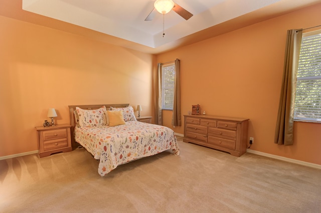 carpeted bedroom with ceiling fan and a raised ceiling