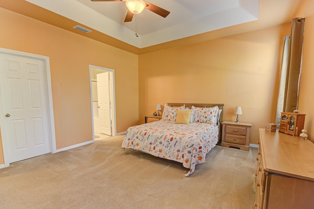 bedroom featuring connected bathroom, light carpet, ceiling fan, and a tray ceiling