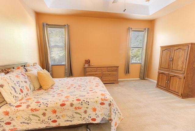 carpeted bedroom featuring multiple windows, ceiling fan, and a tray ceiling