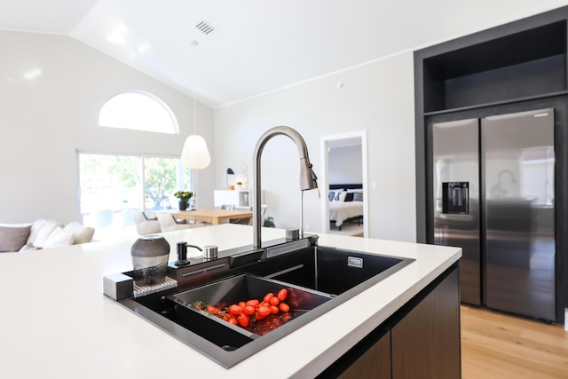 kitchen featuring vaulted ceiling, hanging light fixtures, light hardwood / wood-style floors, stainless steel refrigerator with ice dispenser, and sink