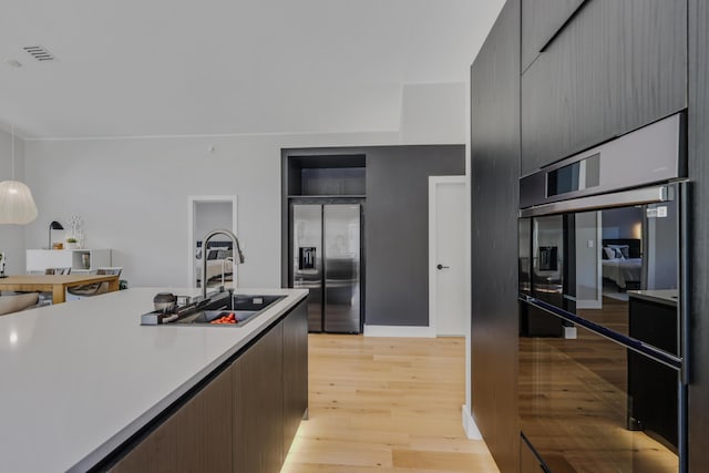 kitchen featuring sink, decorative light fixtures, refrigerator, light hardwood / wood-style floors, and stainless steel refrigerator with ice dispenser