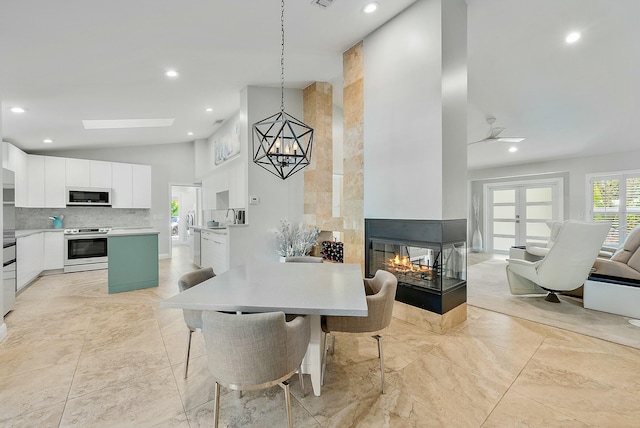 dining area with a multi sided fireplace, sink, high vaulted ceiling, and ceiling fan with notable chandelier