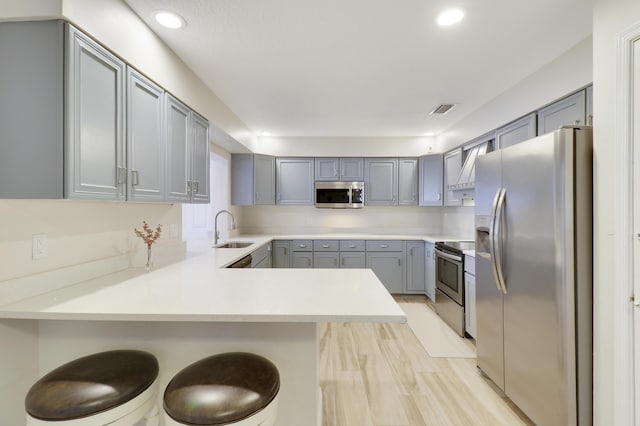 kitchen with sink, a kitchen bar, kitchen peninsula, stainless steel appliances, and light hardwood / wood-style flooring