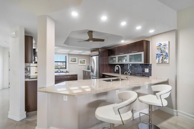 kitchen featuring a breakfast bar, stainless steel refrigerator, sink, decorative backsplash, and kitchen peninsula