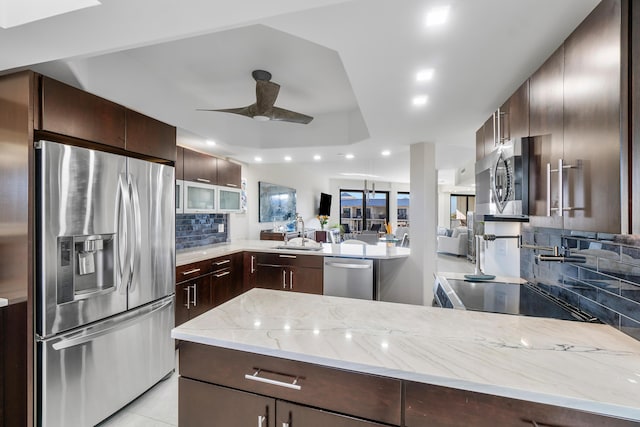 kitchen with appliances with stainless steel finishes, sink, dark brown cabinetry, kitchen peninsula, and light stone countertops