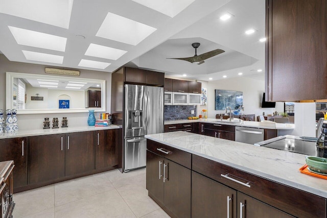 kitchen featuring appliances with stainless steel finishes, decorative backsplash, ceiling fan, dark brown cabinetry, and light stone countertops