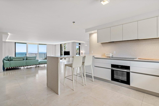 kitchen with stainless steel oven, a kitchen bar, white cabinets, kitchen peninsula, and plenty of natural light