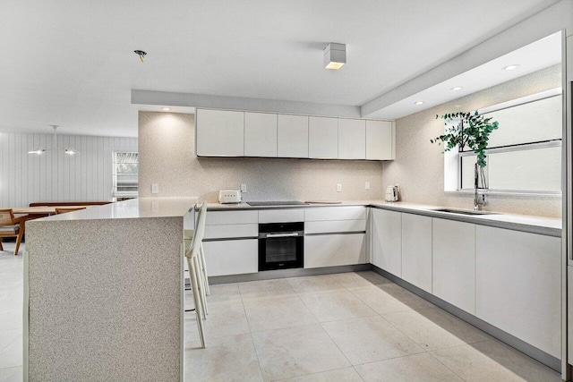 kitchen featuring white cabinets, sink, wall oven, kitchen peninsula, and light tile patterned floors