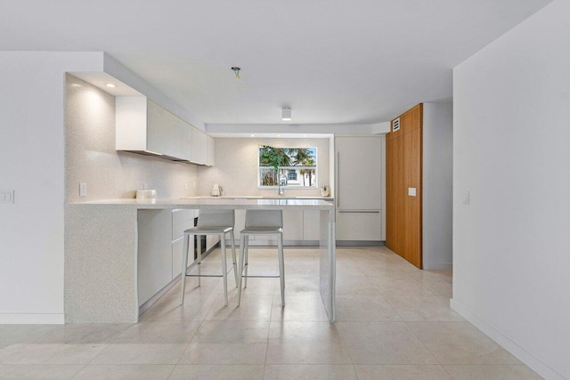 kitchen featuring a kitchen bar, light tile patterned floors, white cabinets, and kitchen peninsula