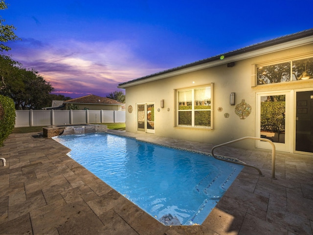 pool at dusk with pool water feature, a patio area, and a hot tub