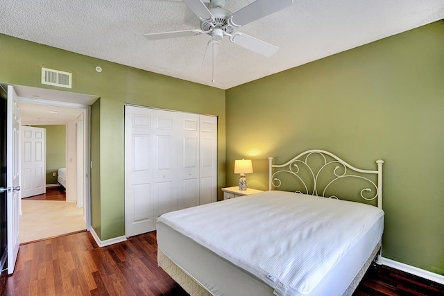 bedroom with a textured ceiling, ceiling fan, a closet, and dark hardwood / wood-style flooring